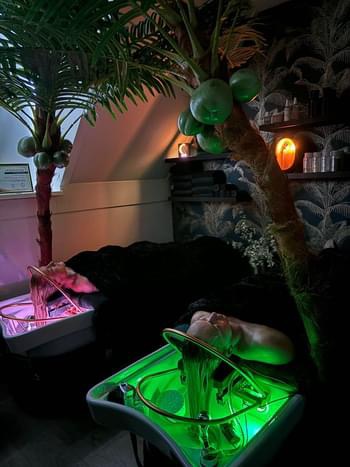 Head spa onder groen sfeerlicht, met een palm boven de wasbak
